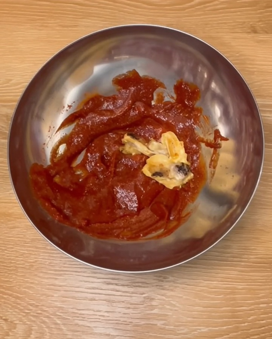 Baked chicken drumsticks being mixed with a rich red Korean-style sauce in a stainless steel bowl.