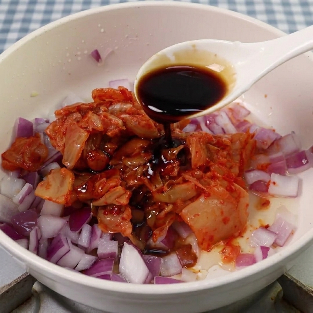Soy sauce, sugar, and Korean spicy paste being added to the kimchi and onion mixture.