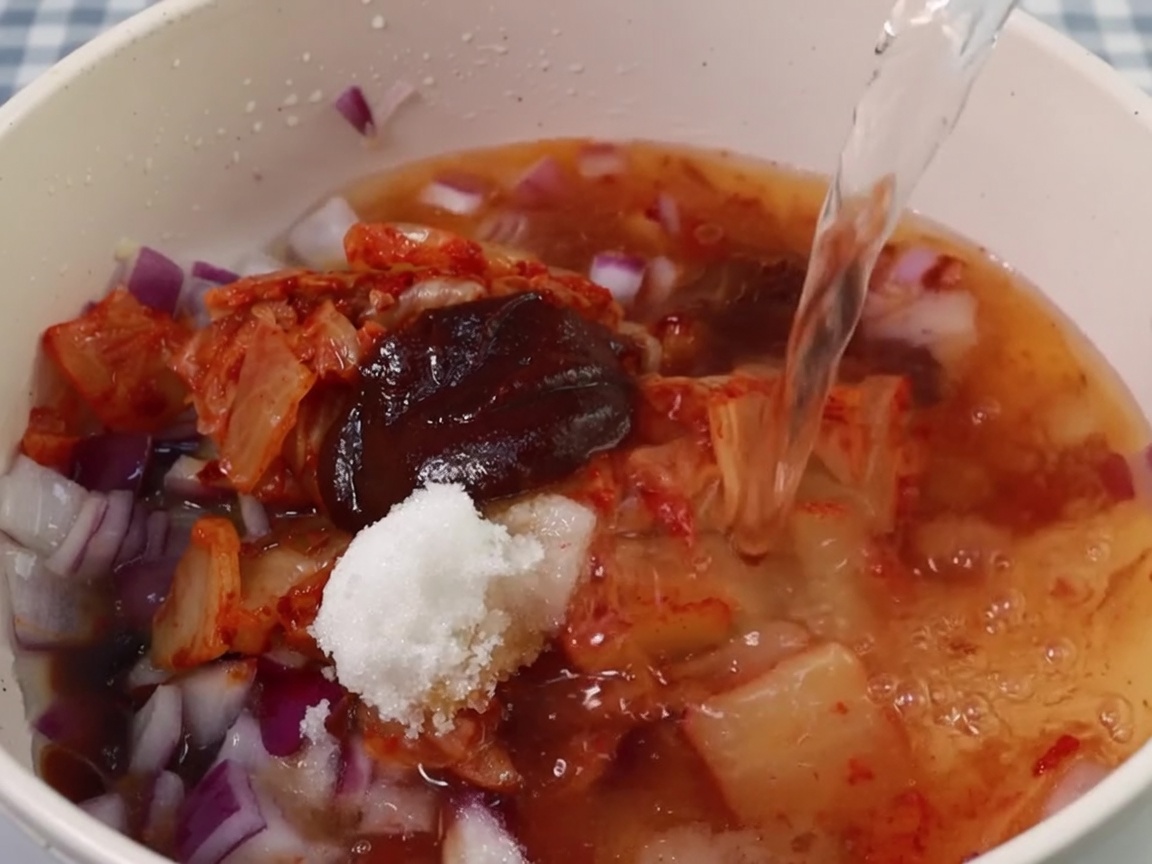 Water being poured into the pot with the kimchi and seasoning base.