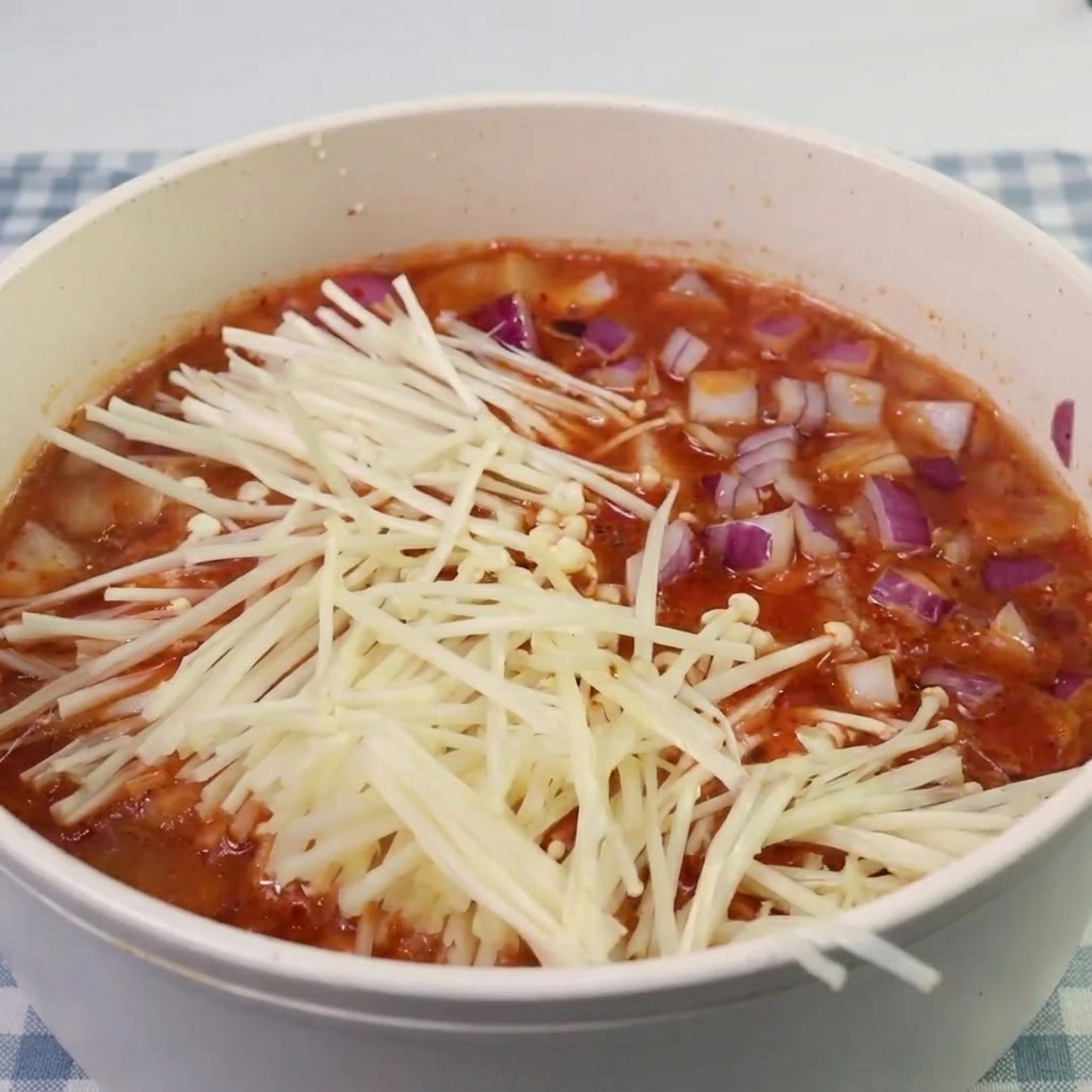 Enoki mushrooms and pieces of spam being added to the simmering kimchi soup.