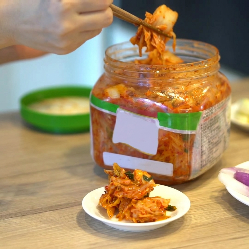 A portion of Korean kimchi being lifted from a container with chopsticks.