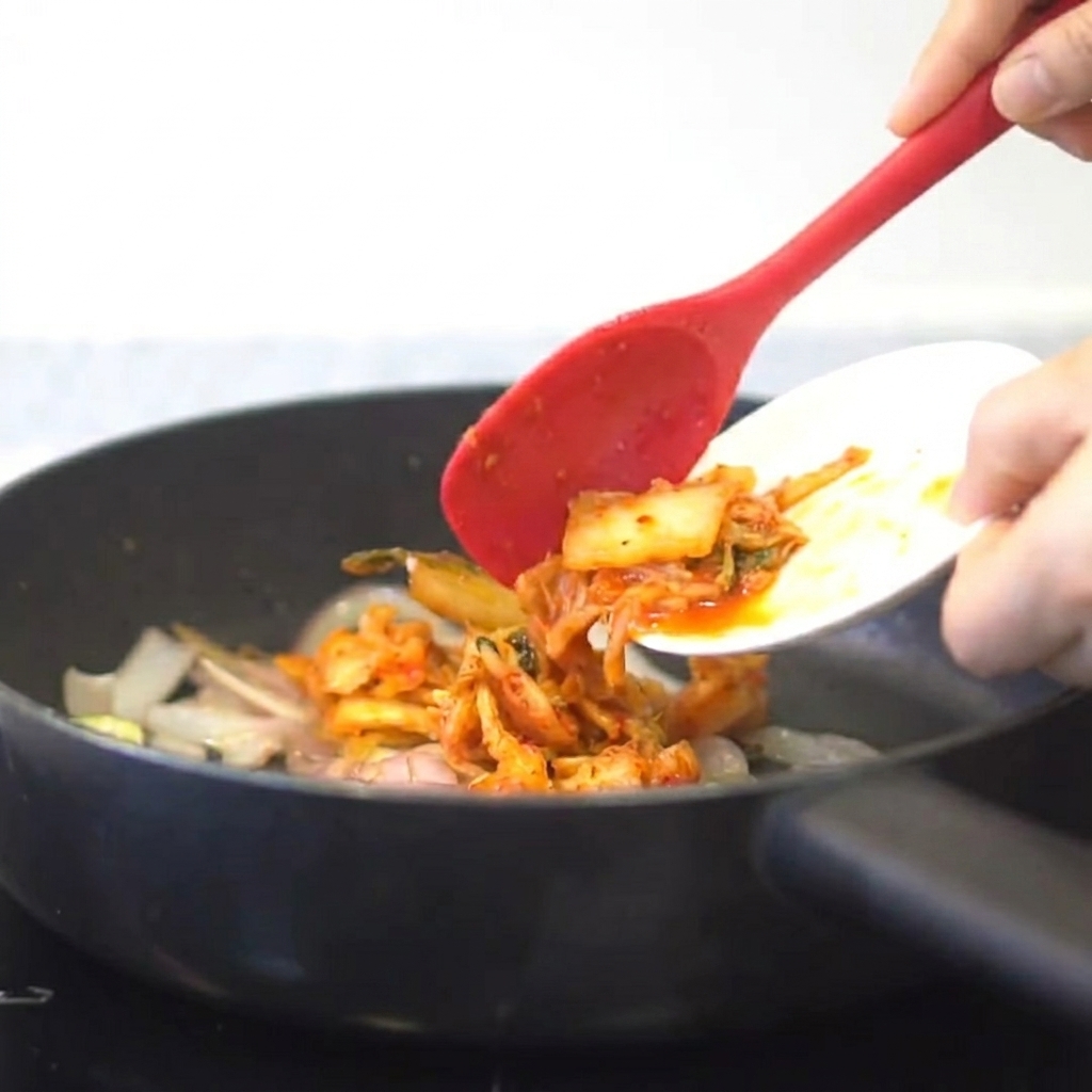 Kimchi being added to a pan with sautéed onions and garlic.