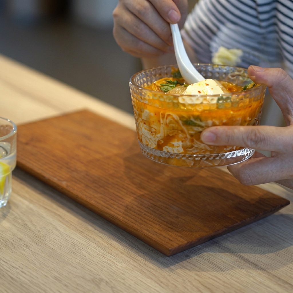 Fresh enoki mushrooms being placed into the pot with the kimchi soup base.