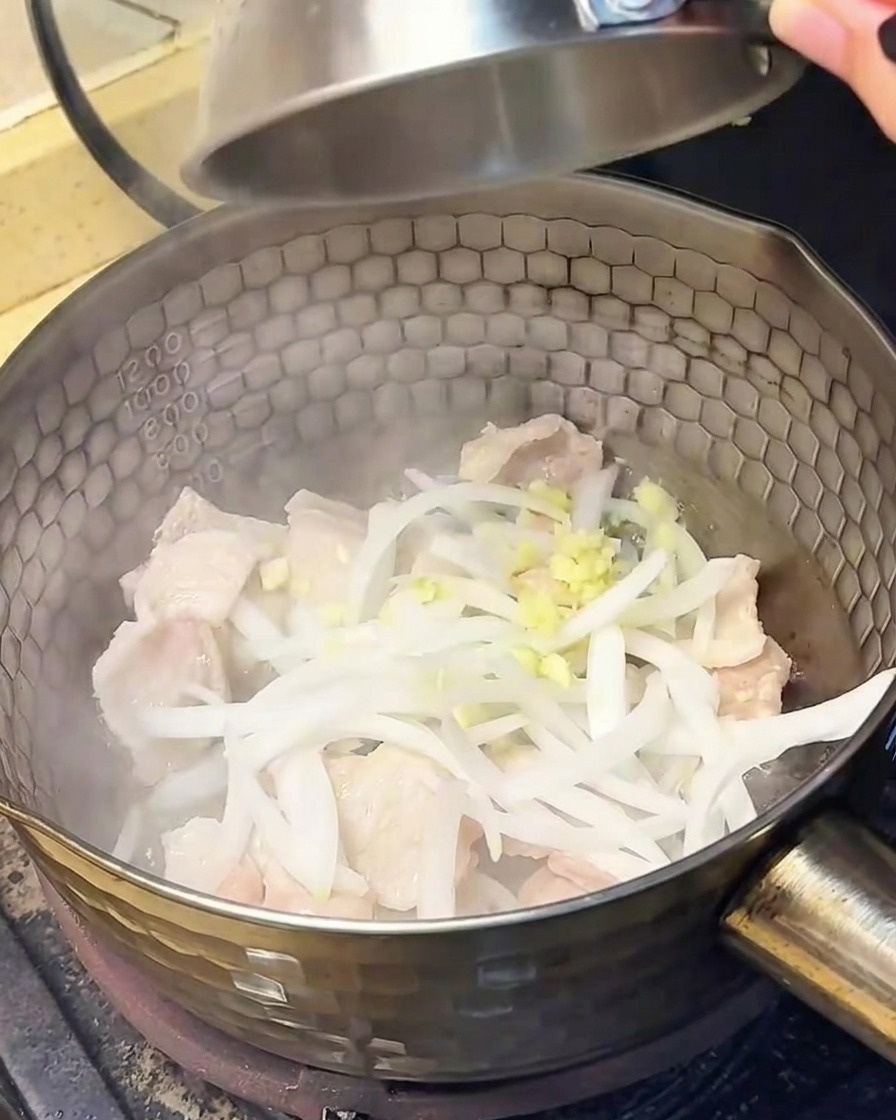 Onion slices and minced garlic being tossed into the pot with the cooked pork belly.