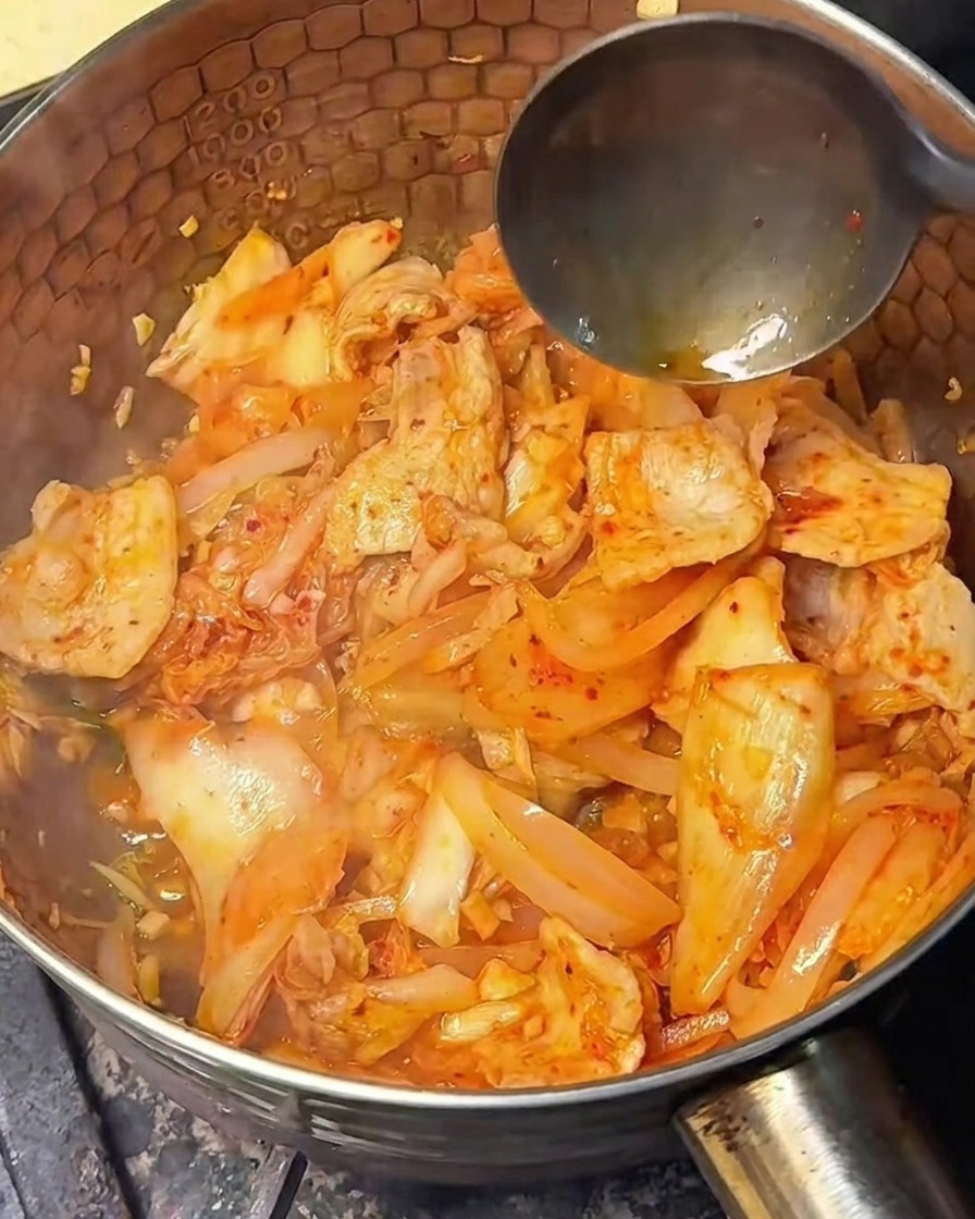 Light soy sauce being poured into the stir-fried kimchi and pork mixture.