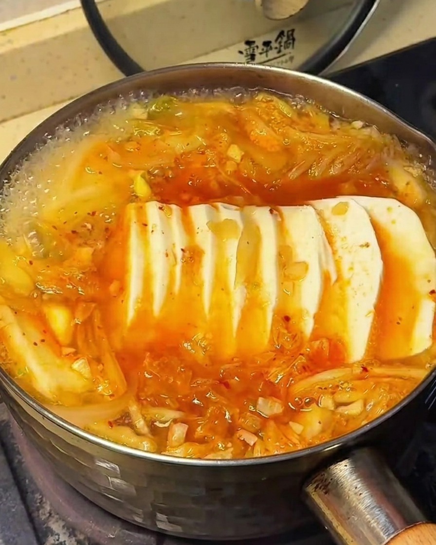 The surface of the kimchi soup with tofu, showing the moment seasonings are sprinkled onto the ingredients.
