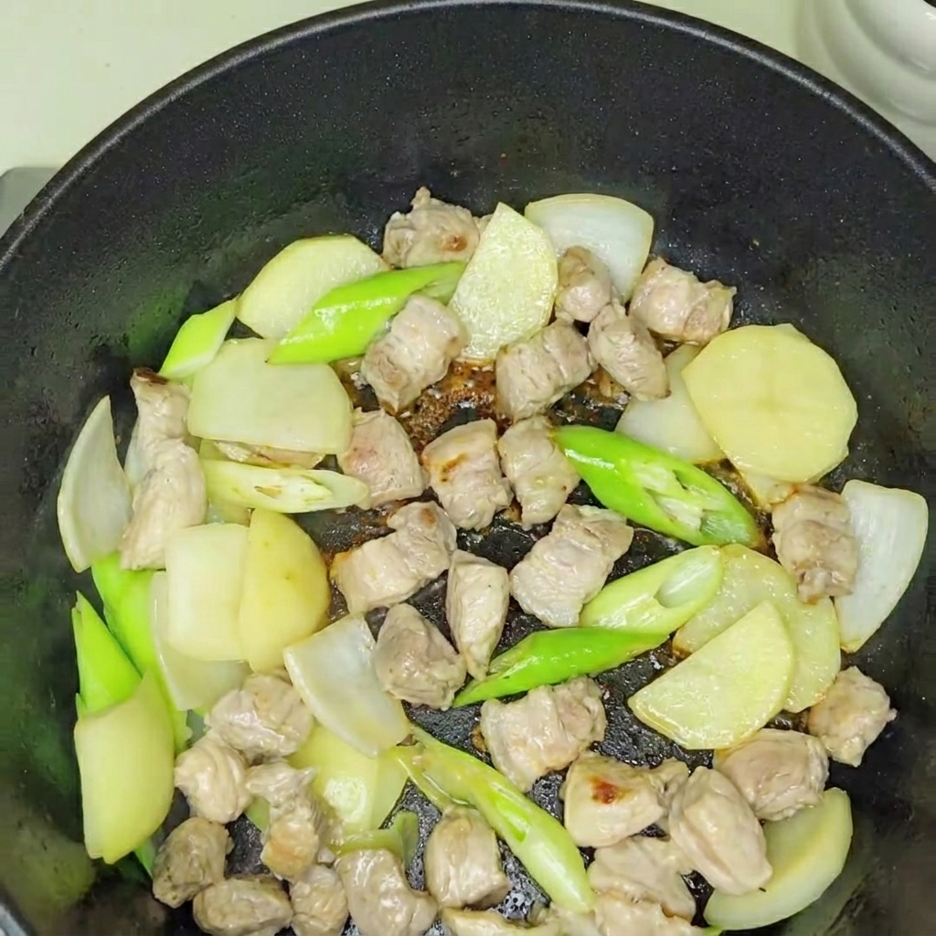 Freshly added kimchi being stirred into the sautéed pork and onion base.