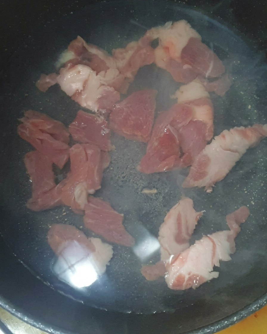 Pork pieces submerged in water in a cooking pot with a spoonful of salted shrimp added.