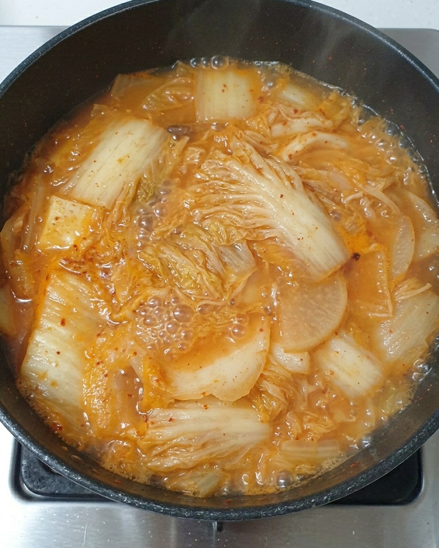 A spoonful of light soy sauce being poured into the simmering kimchi stew.