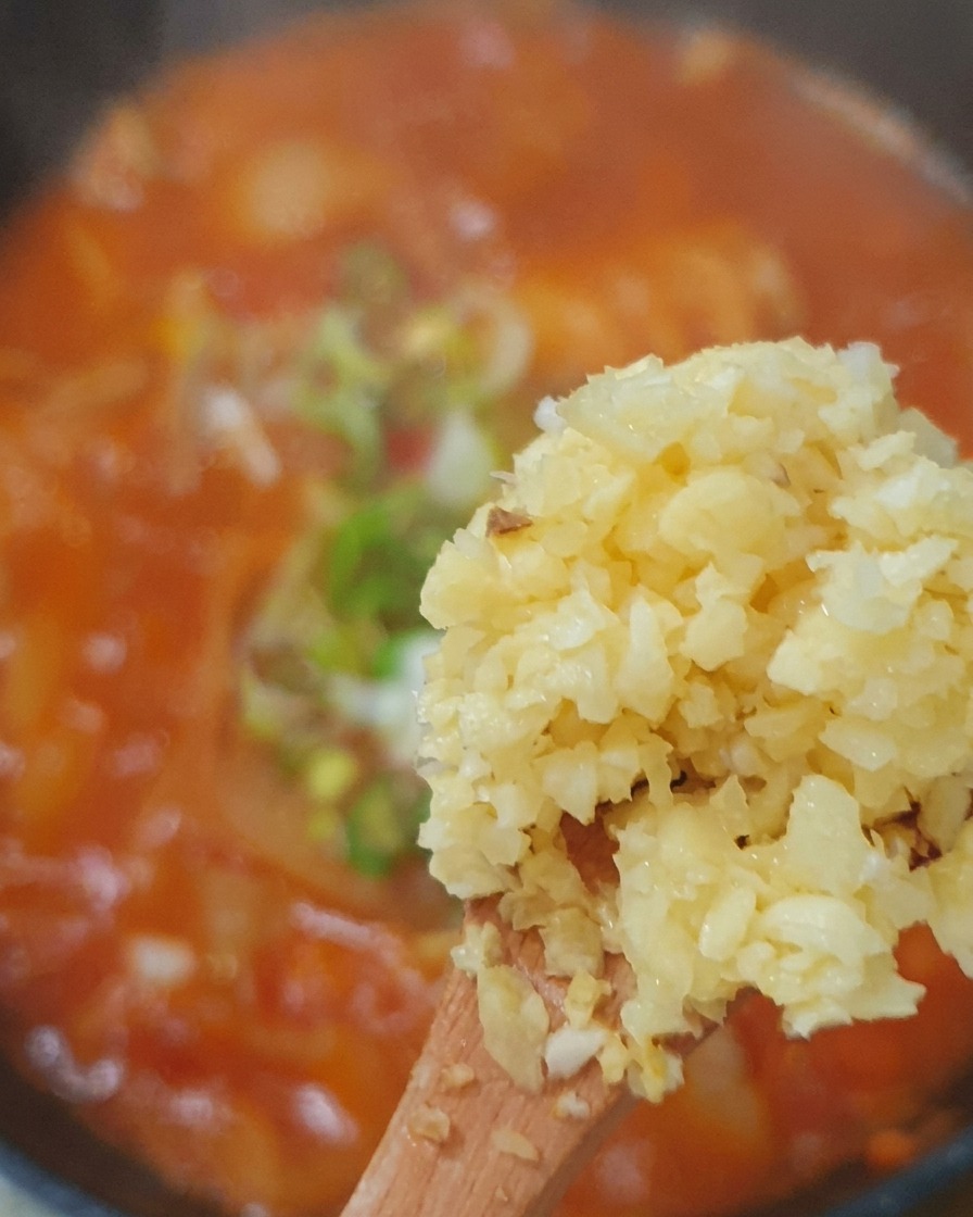 Freshly minced garlic, sliced green onions, and green chili pieces being added to the simmering kimchi broth.