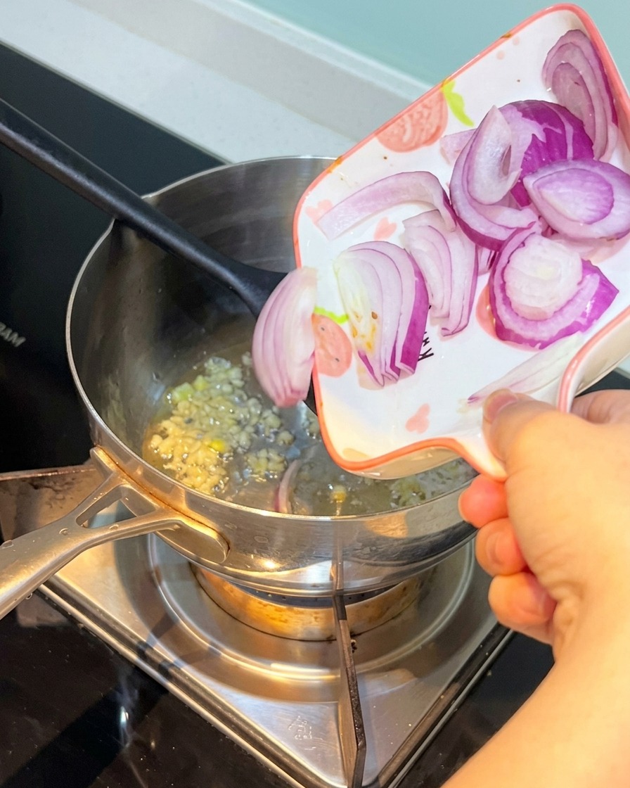 Sliced red onion being added to the pot with garlic.
