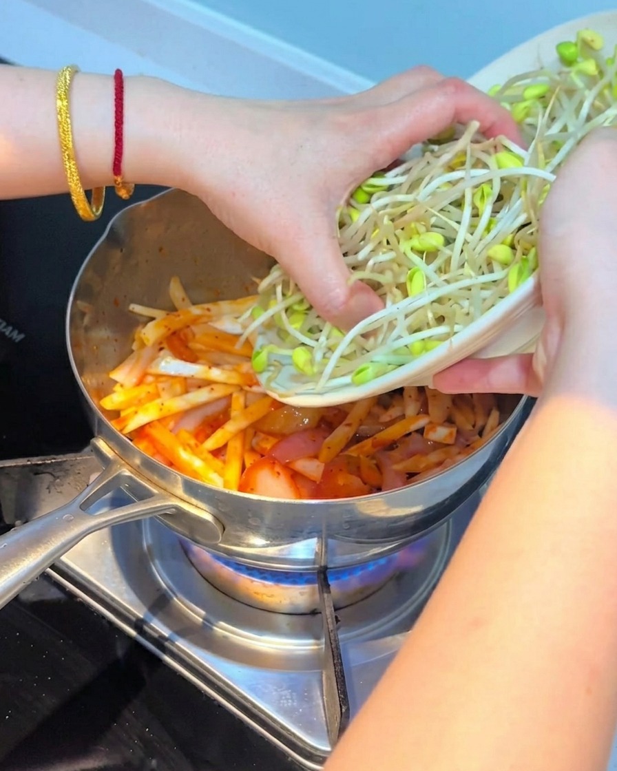 Fresh bean sprouts being layered on top of the kimchi and mushroom mixture.
