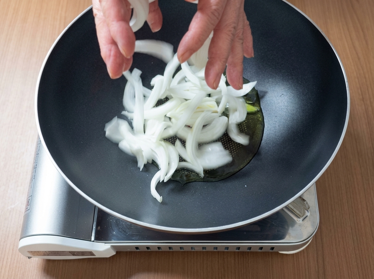Pork pieces and sliced onions sizzling together in a pan with oil.