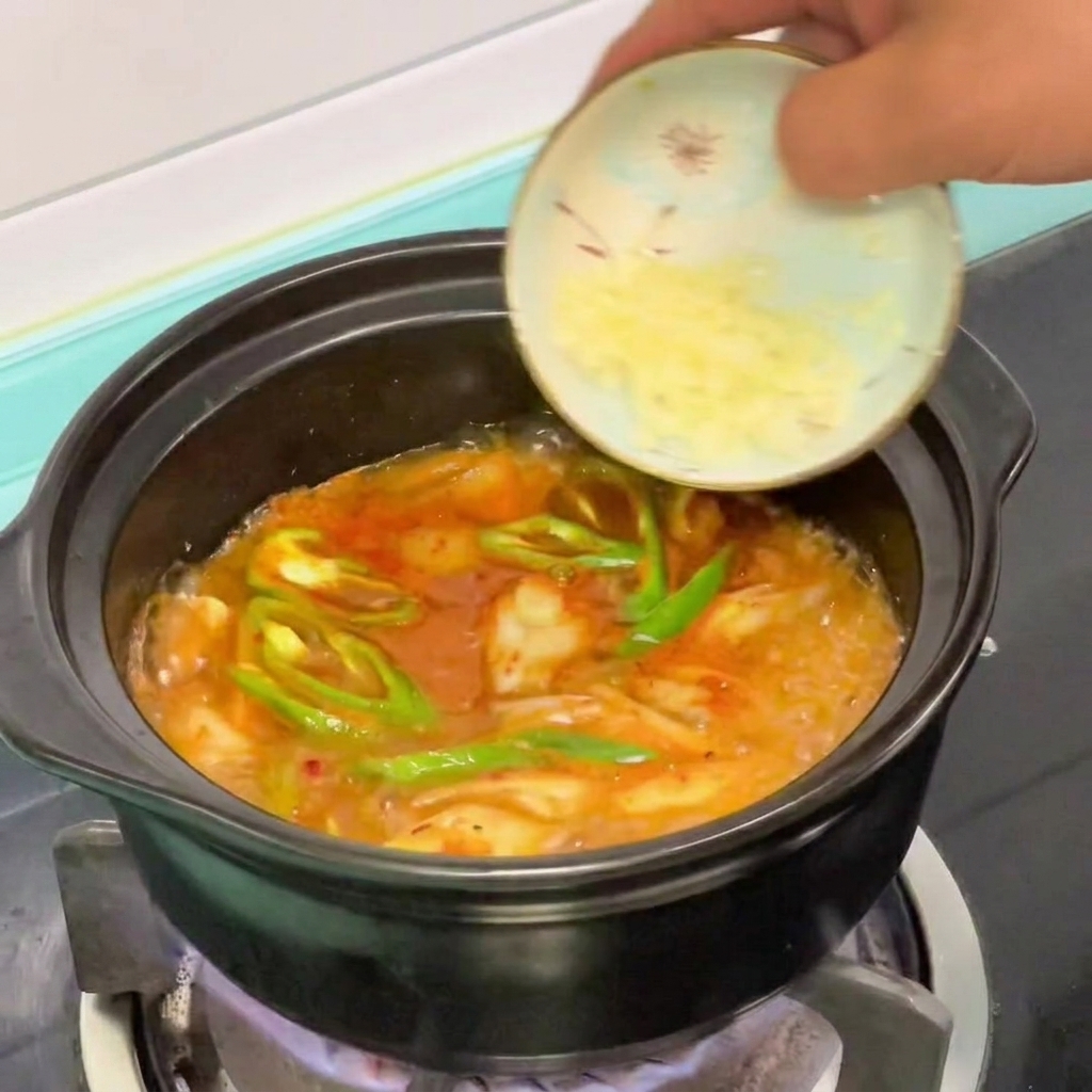 Minced garlic being added to a simmering pot of Korean soft tofu stew.