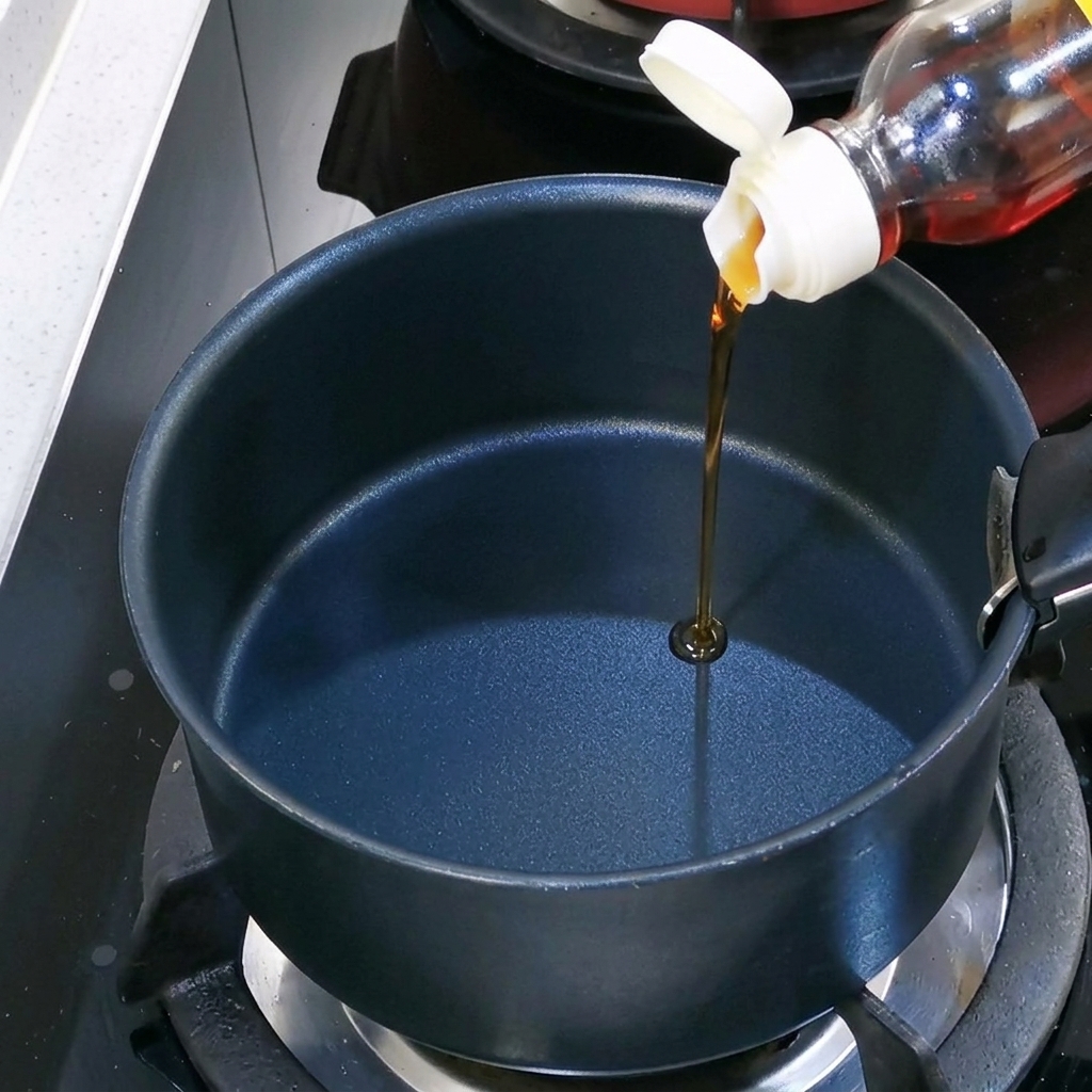 Sesame oil being poured into an empty black pot on the stove.