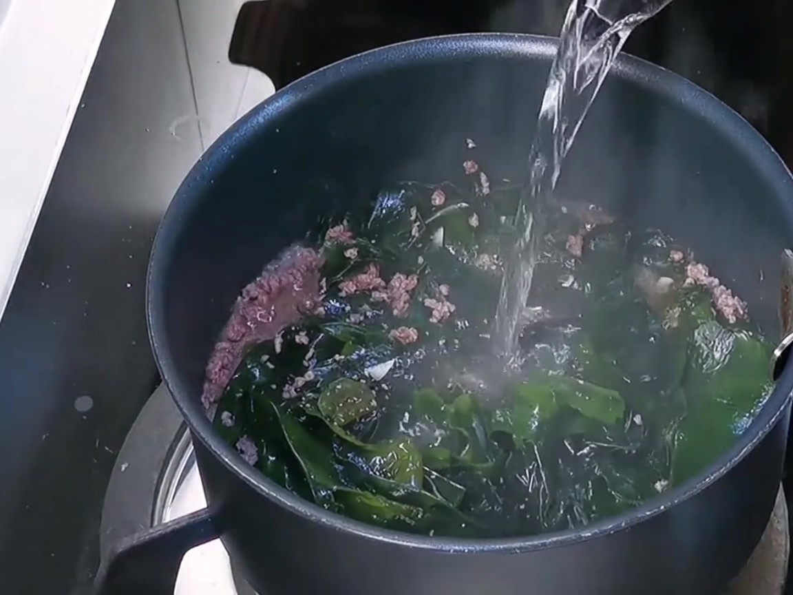 Fresh water being poured into the pot over the beef and wakame base.