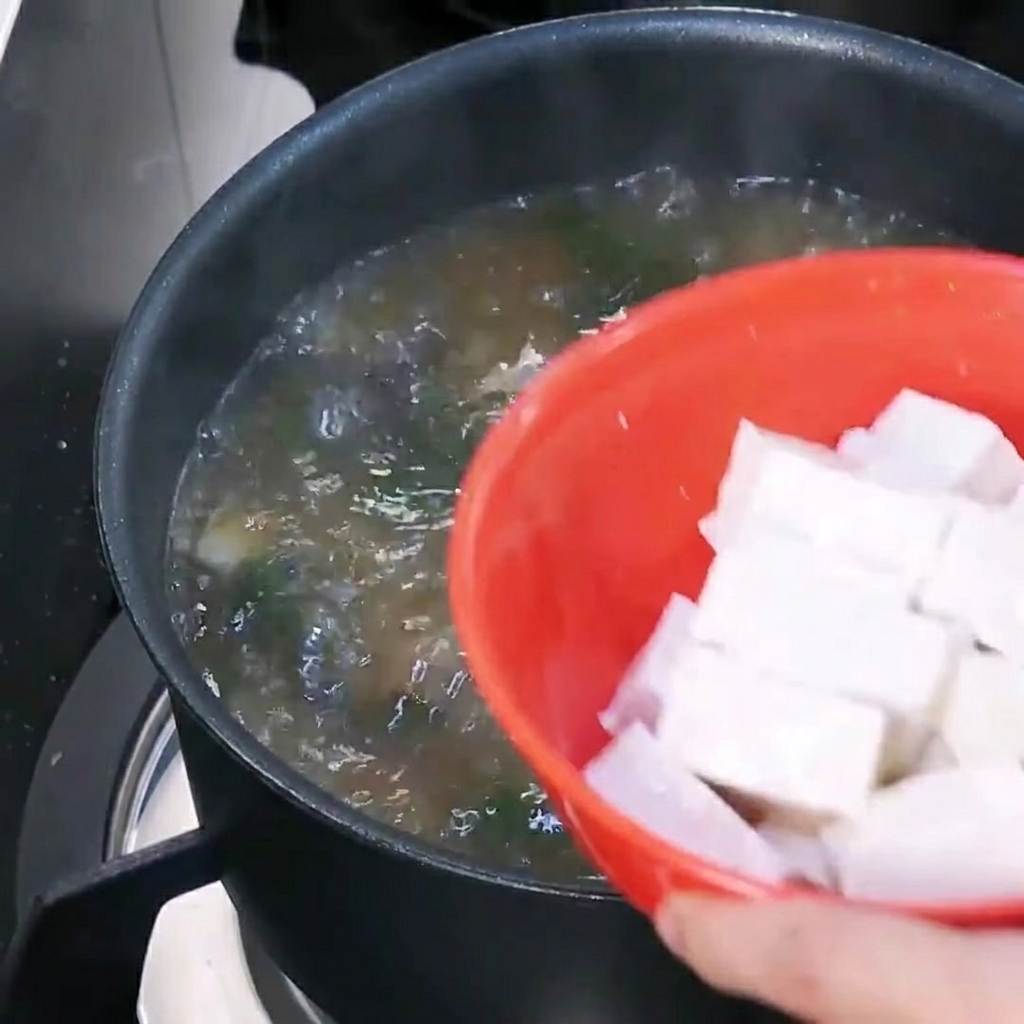 Cubed tofu being added to a pot of boiling Korean soybean paste soup.