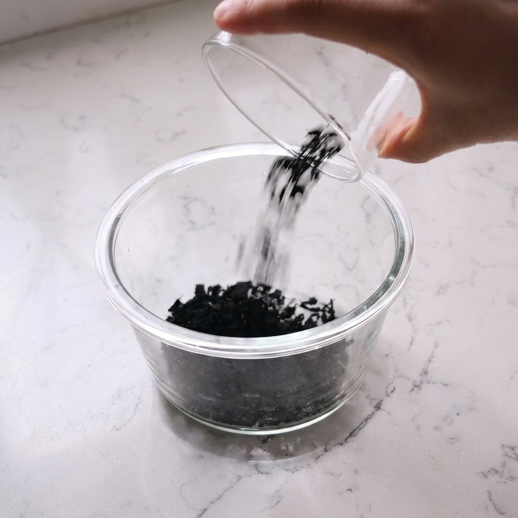 Dry wakame seaweed being soaked in a glass bowl filled with water.