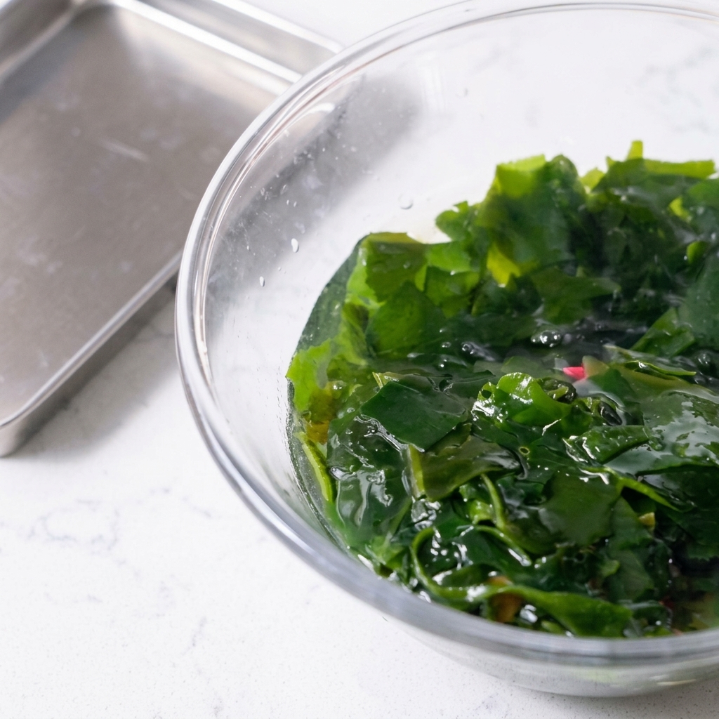 Rehydrated wakame seaweed being lifted from a bowl using a pink slotted spoon.