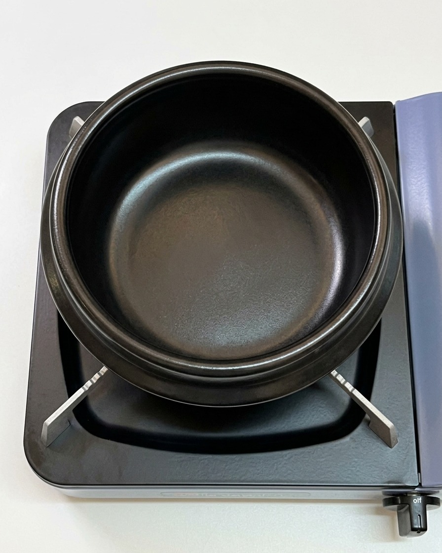 Sesame oil pooling in the bottom of a black earthenware pot on a stove.