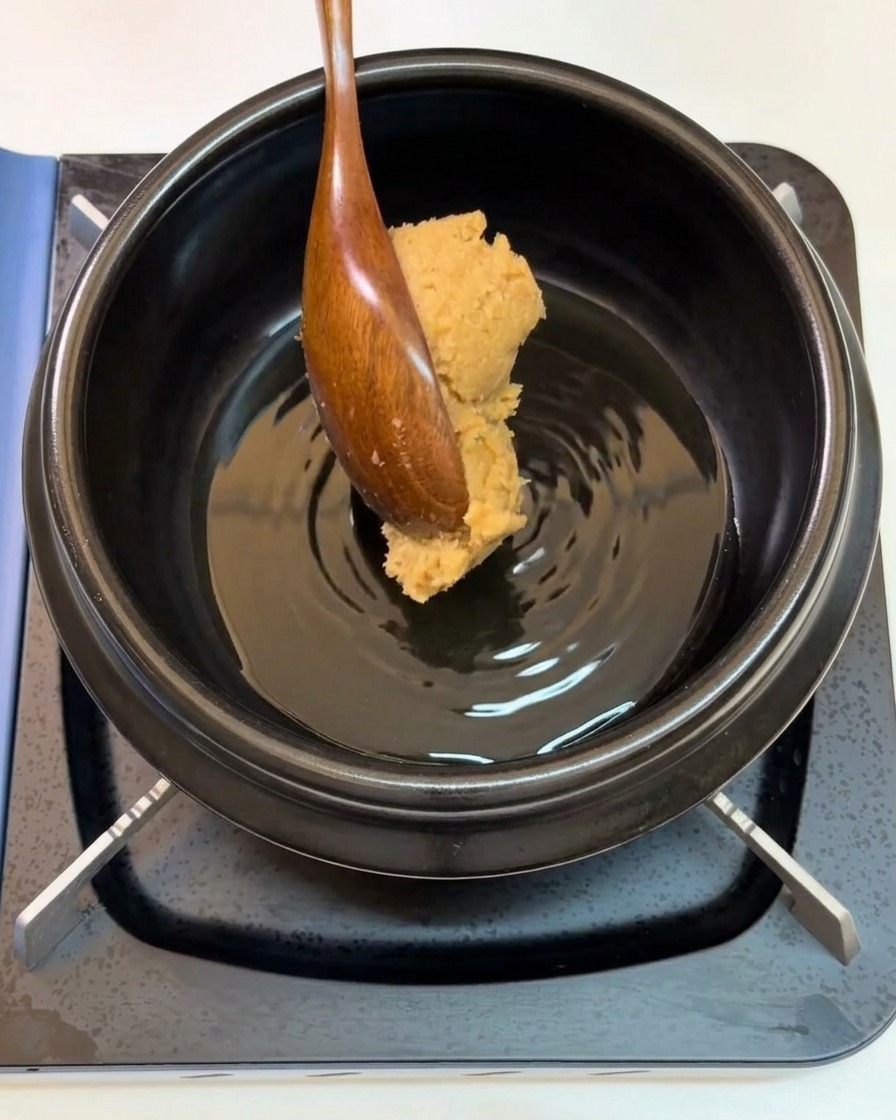 A wooden spoon adding a dollop of soybean paste into a pot.