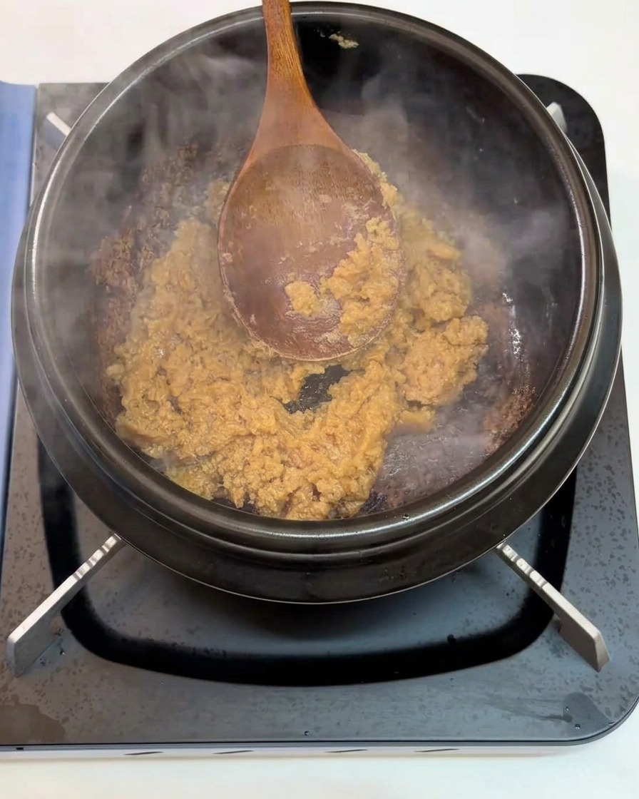Minced garlic being stirred into the sautéing soybean paste in the pot.