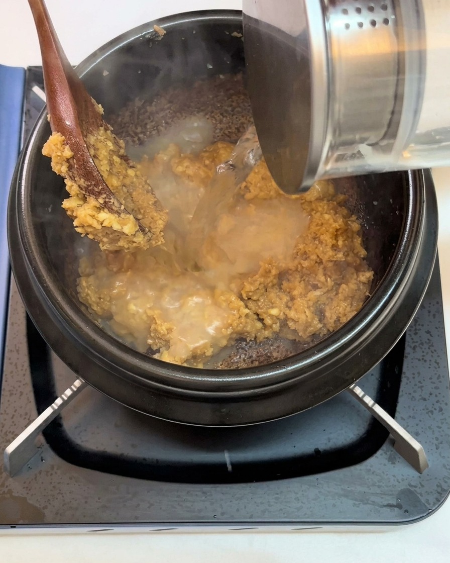 Water being poured into the pot over the fried soybean paste and garlic mixture.