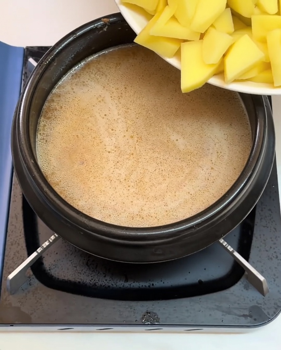 Potatoes and various other chopped ingredients being added into the boiling broth.