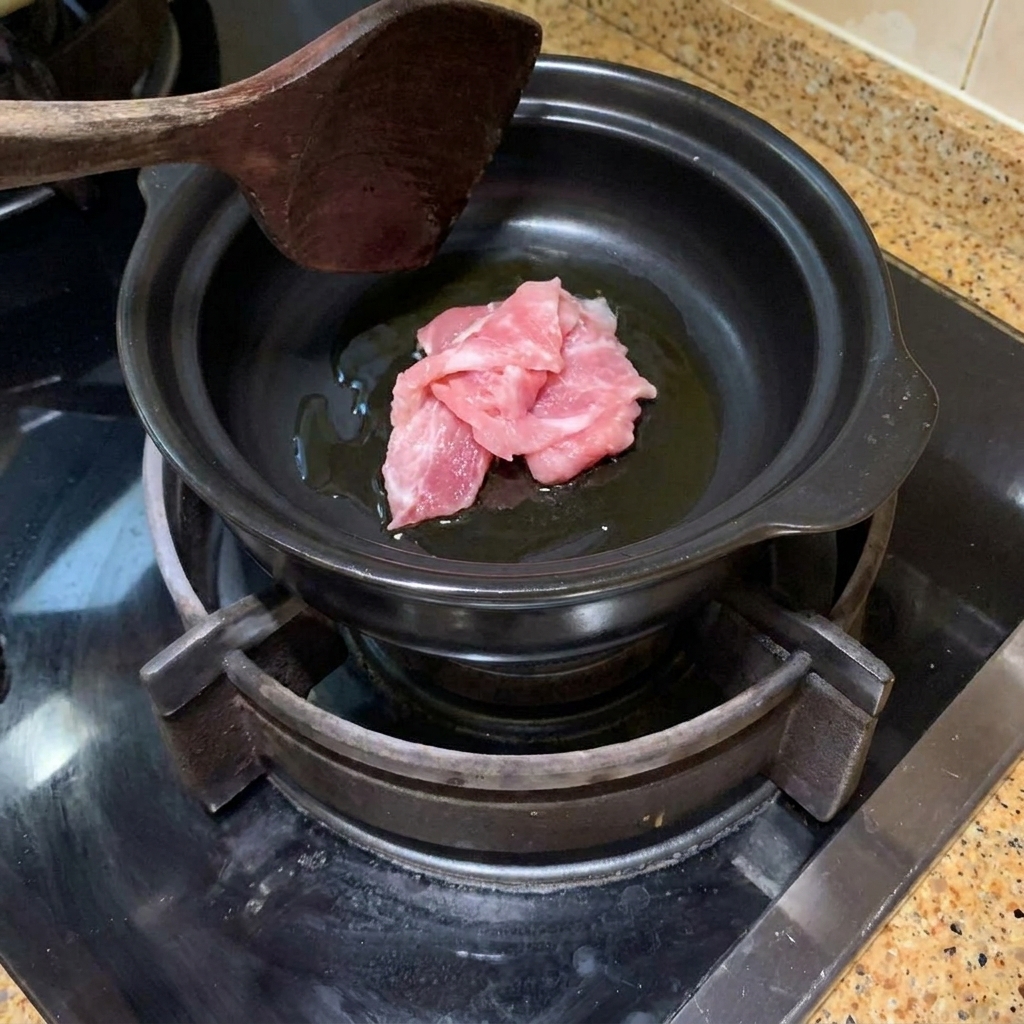 Slices of pork being stir-fried in a hot clay pot with oil.