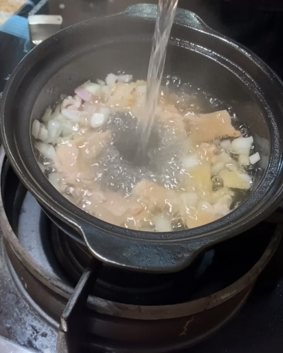 Water being poured into the clay pot containing the pork and aromatics.