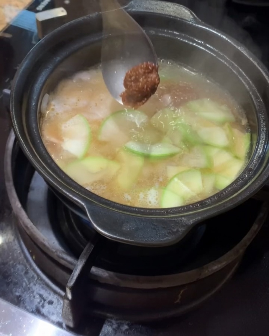 Korean soybean paste and chili paste being added into the simmering pot.