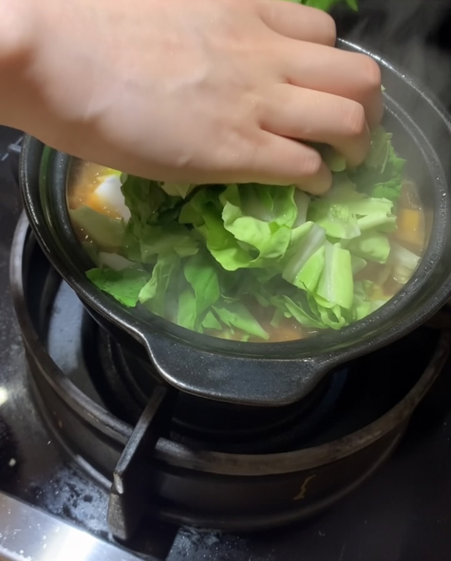Fresh leafy greens being added to the stew.