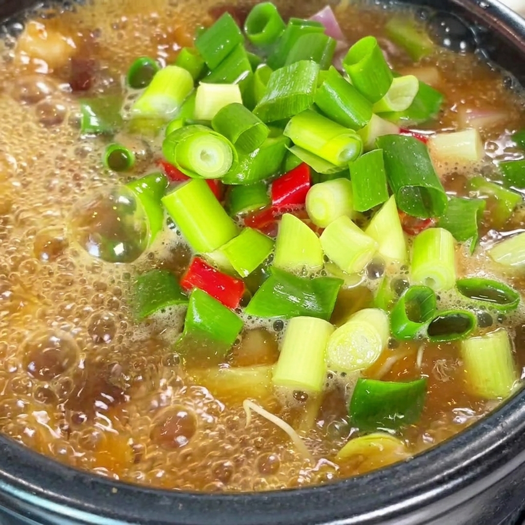 A close-up of the simmering soybean paste stew being seasoned with red chili powder and beef powder.