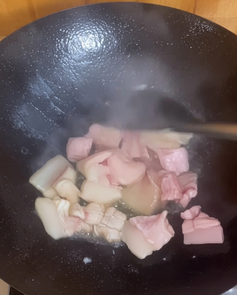 Pork belly pieces sizzling and browning in a hot wok.