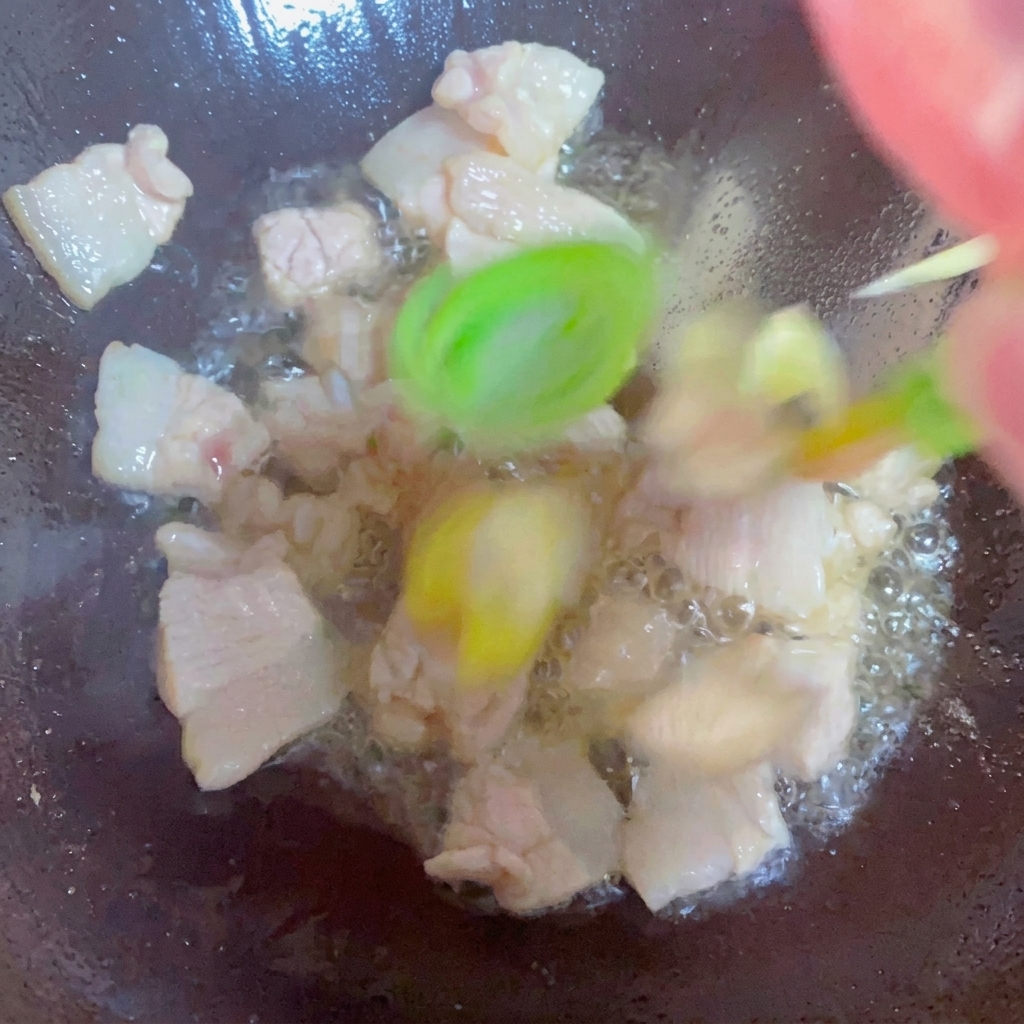 Green onions, ginger, and garlic being stir-fried with pork belly in a wok.