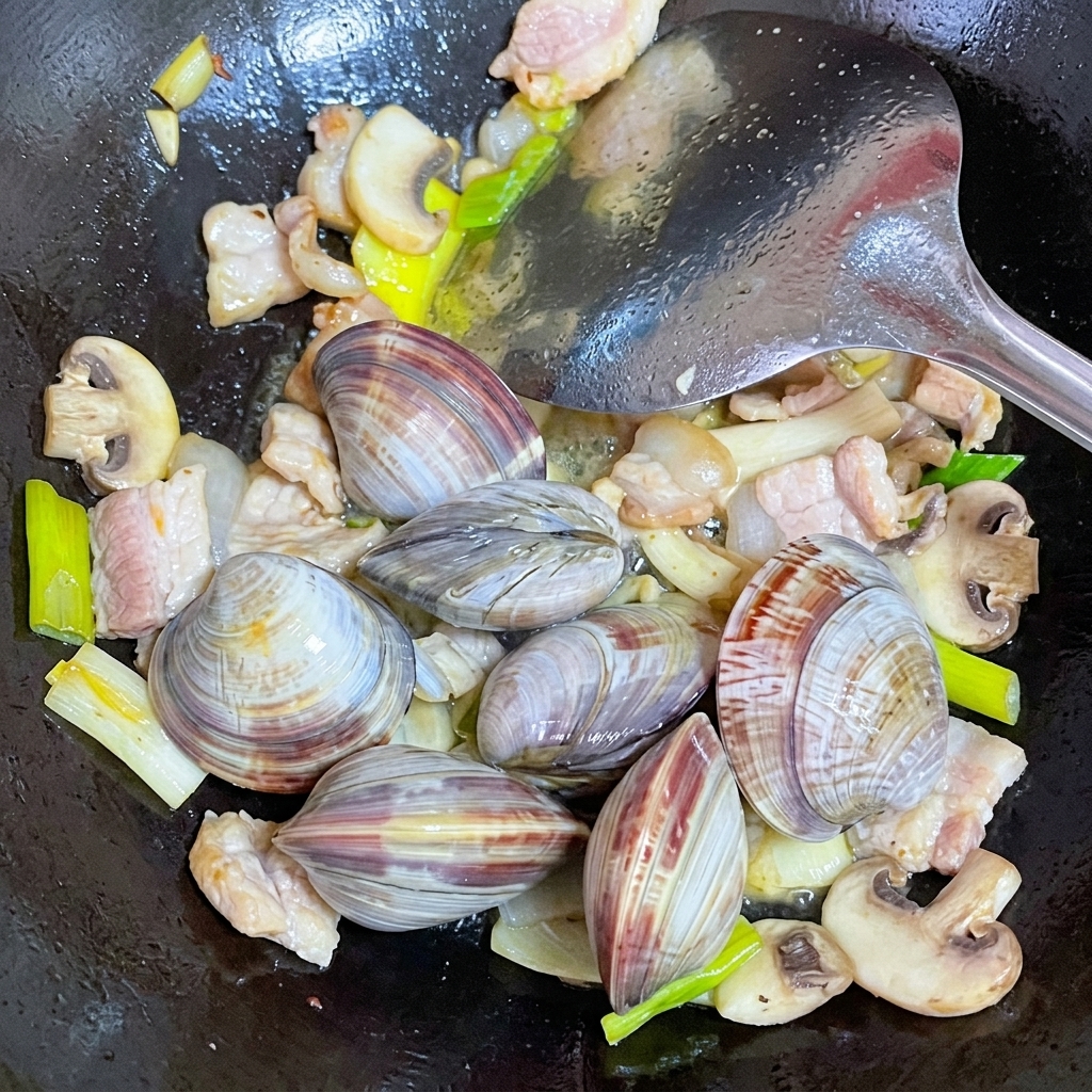 Freshly cleaned clams added into a wok with stir-fried pork and mushrooms.