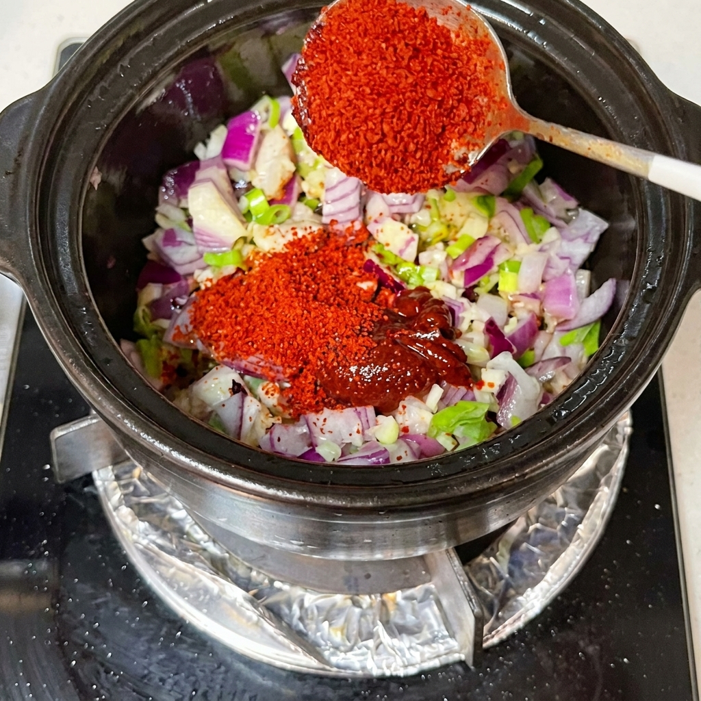 Soy sauce and kimchi being stirred into a pot with diced onions and aromatics.