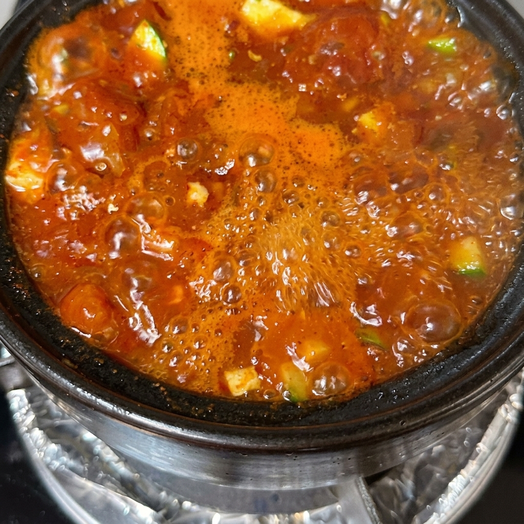 A finished pot of tofu soup garnished with sliced green onions and red chili peppers.