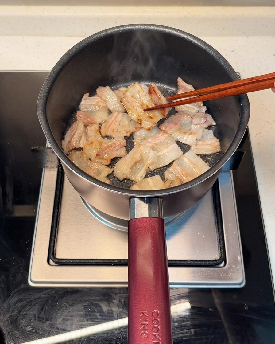 Pork belly slices browning evenly in a hot pot, with rendered fat visible.