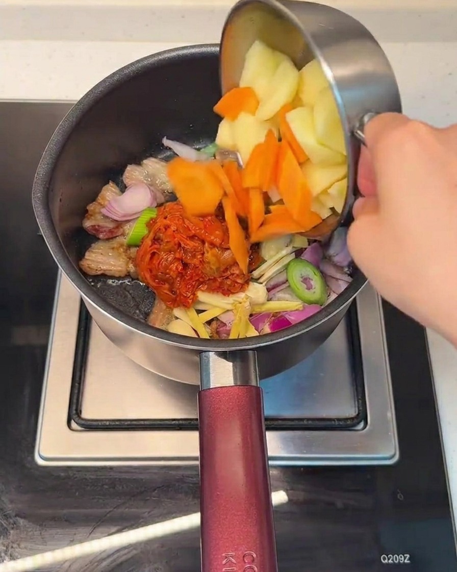 Adding chopped carrots and potatoes into the pot containing the pork and kimchi mixture.