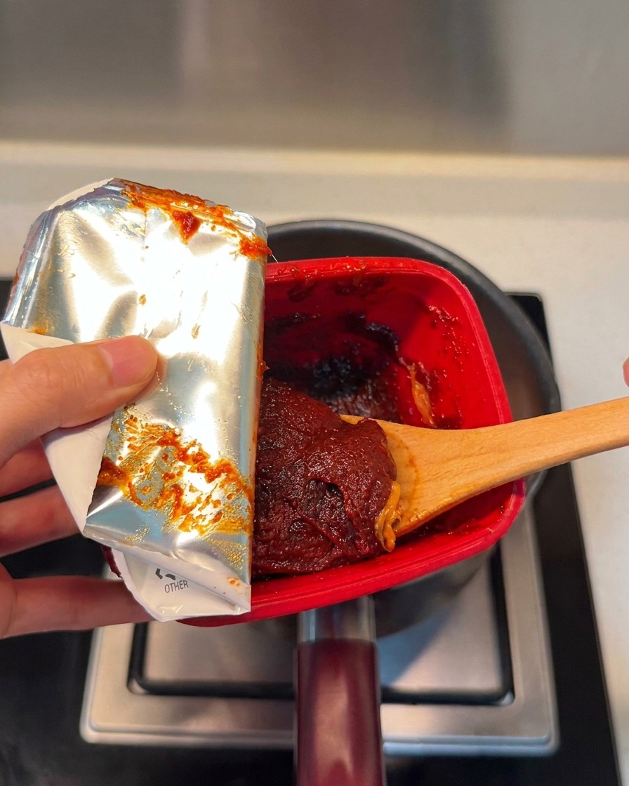 A spoonful of rich, red Korean chili paste being added into the pot.
