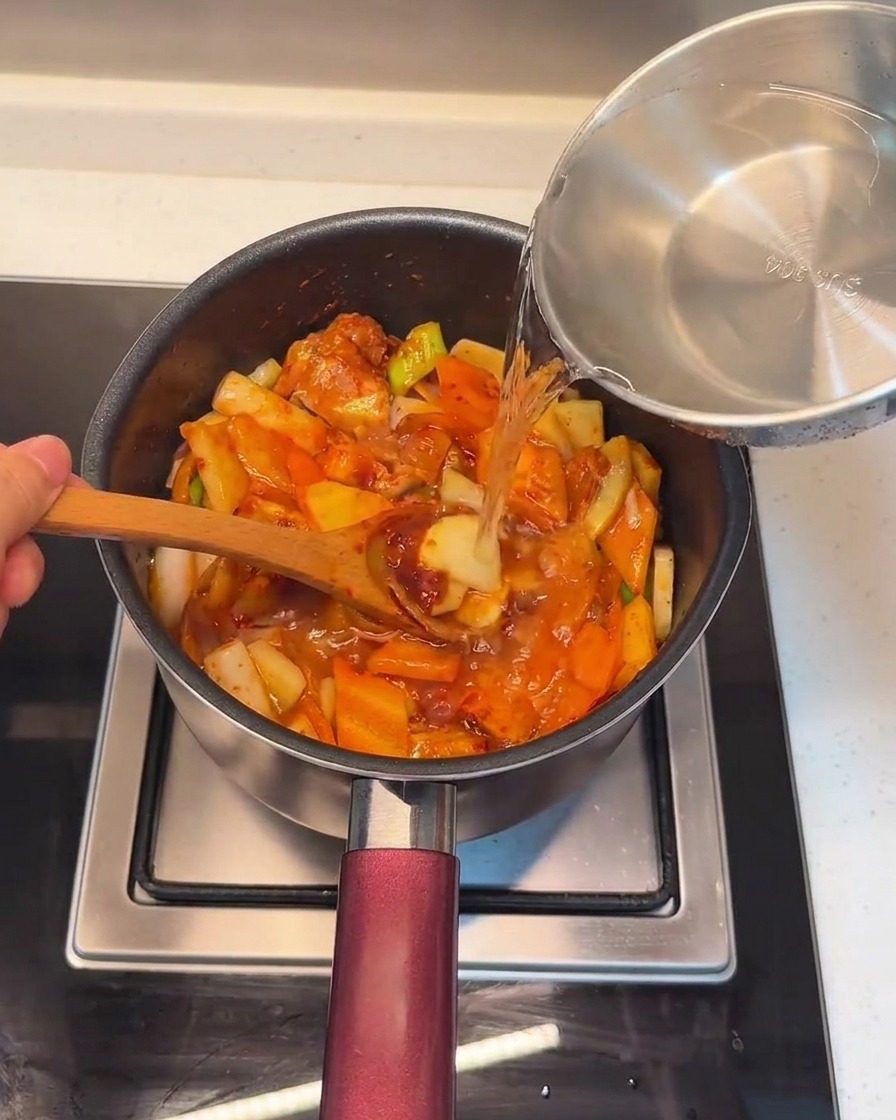 Pouring fresh water into the pot over the combined pork and vegetable mixture.