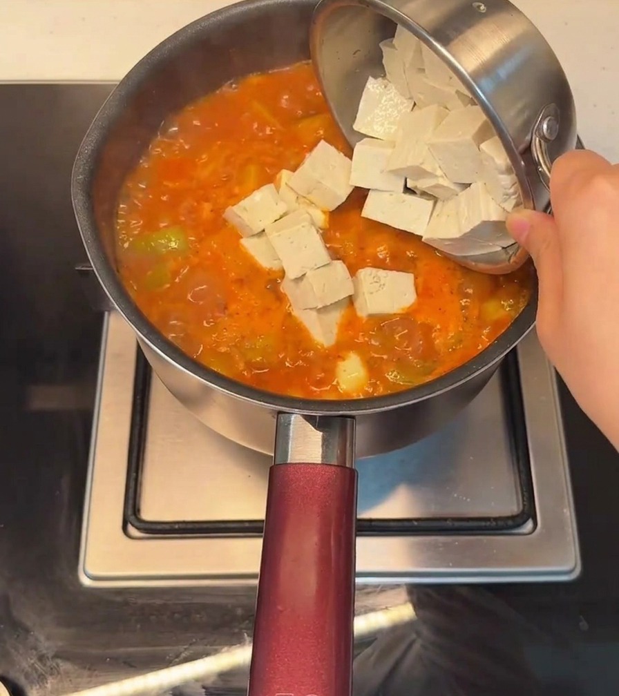 Cubed tofu being added to a pot of bubbling, red Korean-style spicy stew.