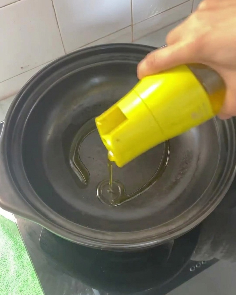 Cooking oil being poured into an empty, heated clay pot.