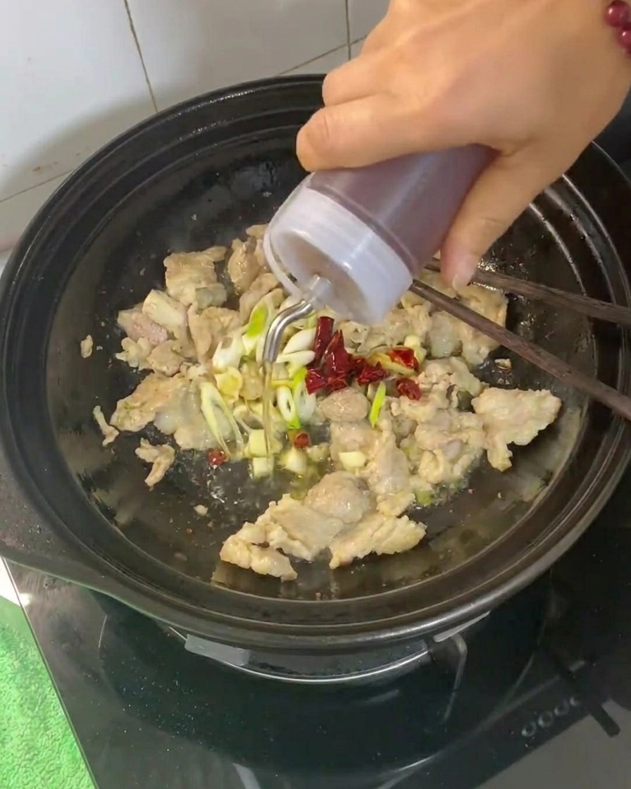 Cooking wine being poured into the clay pot containing the pork and aromatics.