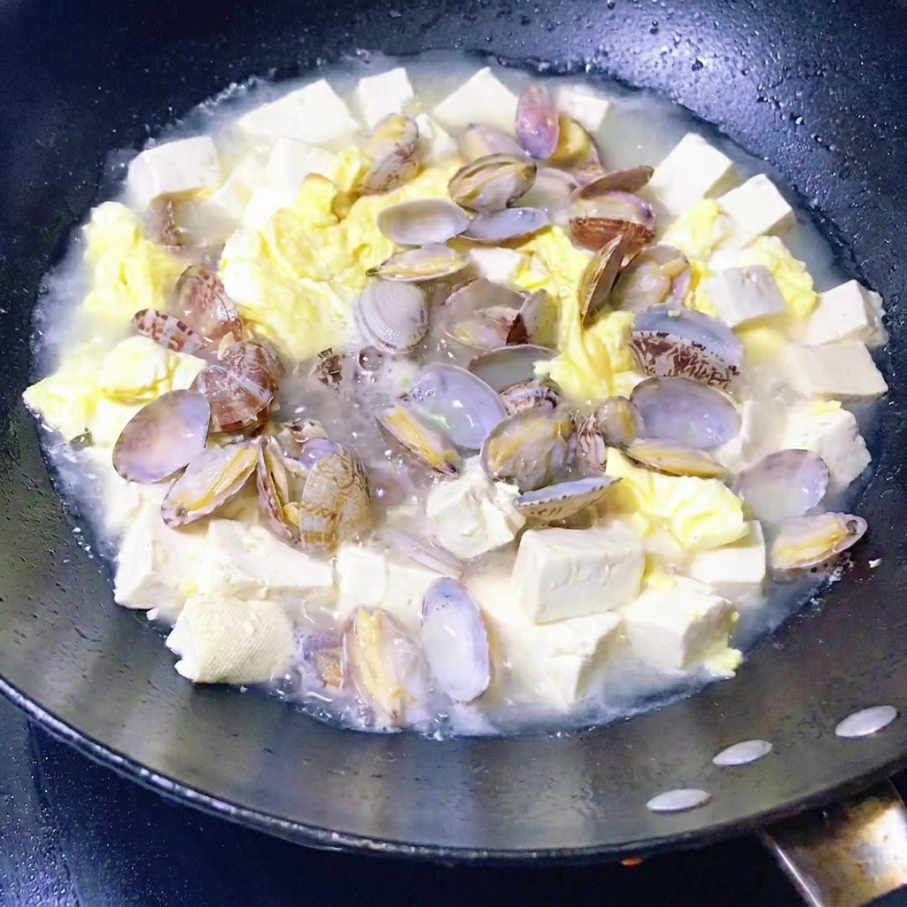 Leafy green vegetables being added to a pan of simmering clam, tofu, and egg stew.