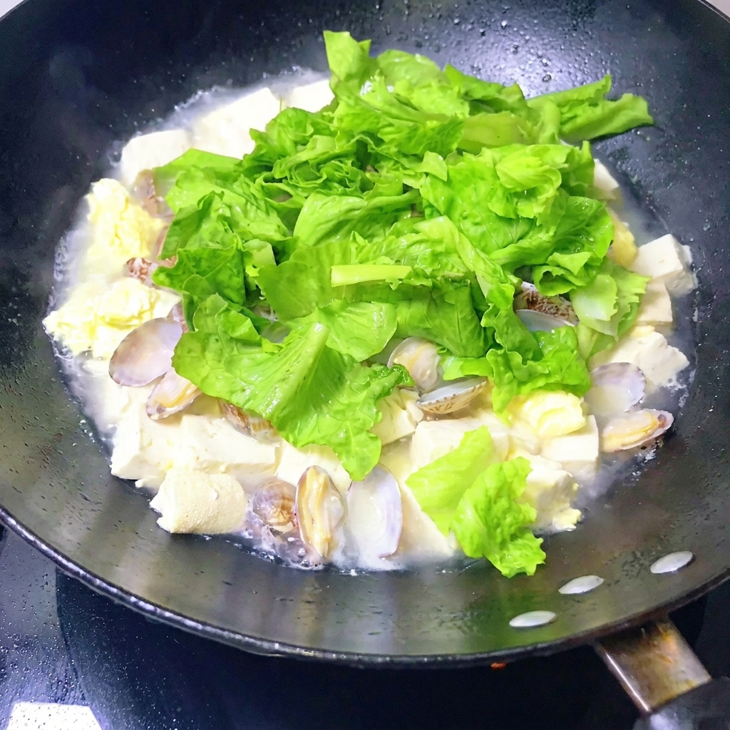 A pan of finished clam and tofu stew being gently stirred with a ladle.