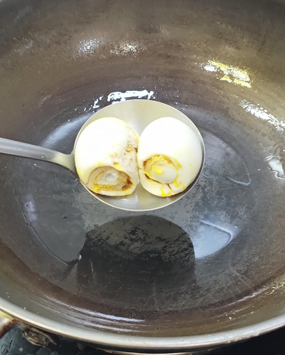 Two salted duck eggs sizzling in a hot wok with oil.
