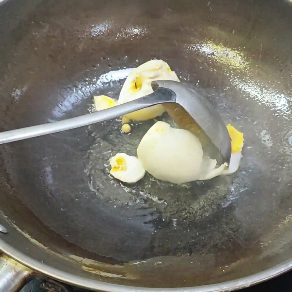 A ladle breaking up salted duck eggs in a wok.