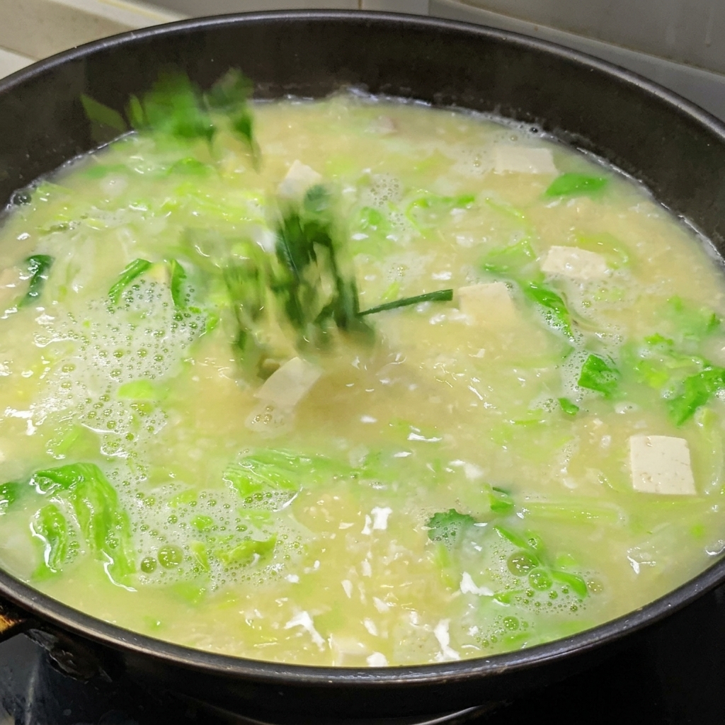 A starch water slurry being poured into a pot of bubbling salted egg and tofu soup to thicken the broth.